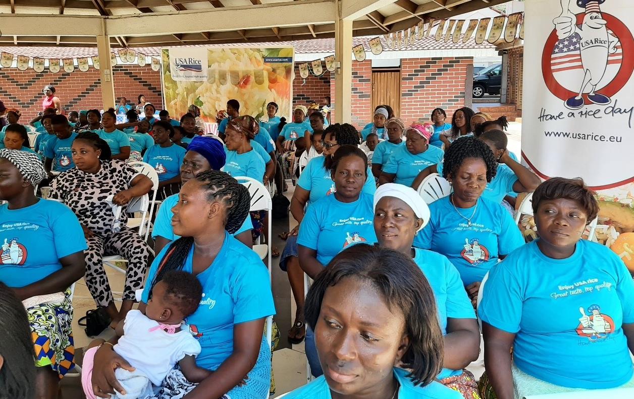 Group of women wearing blue USAR t-shirts sit under large pavilion at a cooking seminar in Takoradi, Ghana