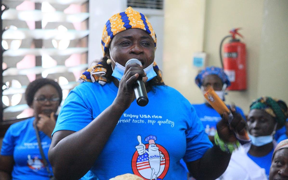 Black woman wearing yellow & blue head scarf and blue t-shirt holding microphone