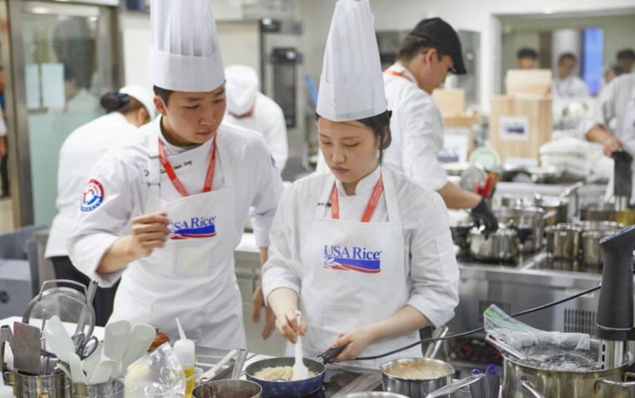 Induction-Cooking-Competition,-2-participants-wearing-USAR-aprons & toques at stove, making rice