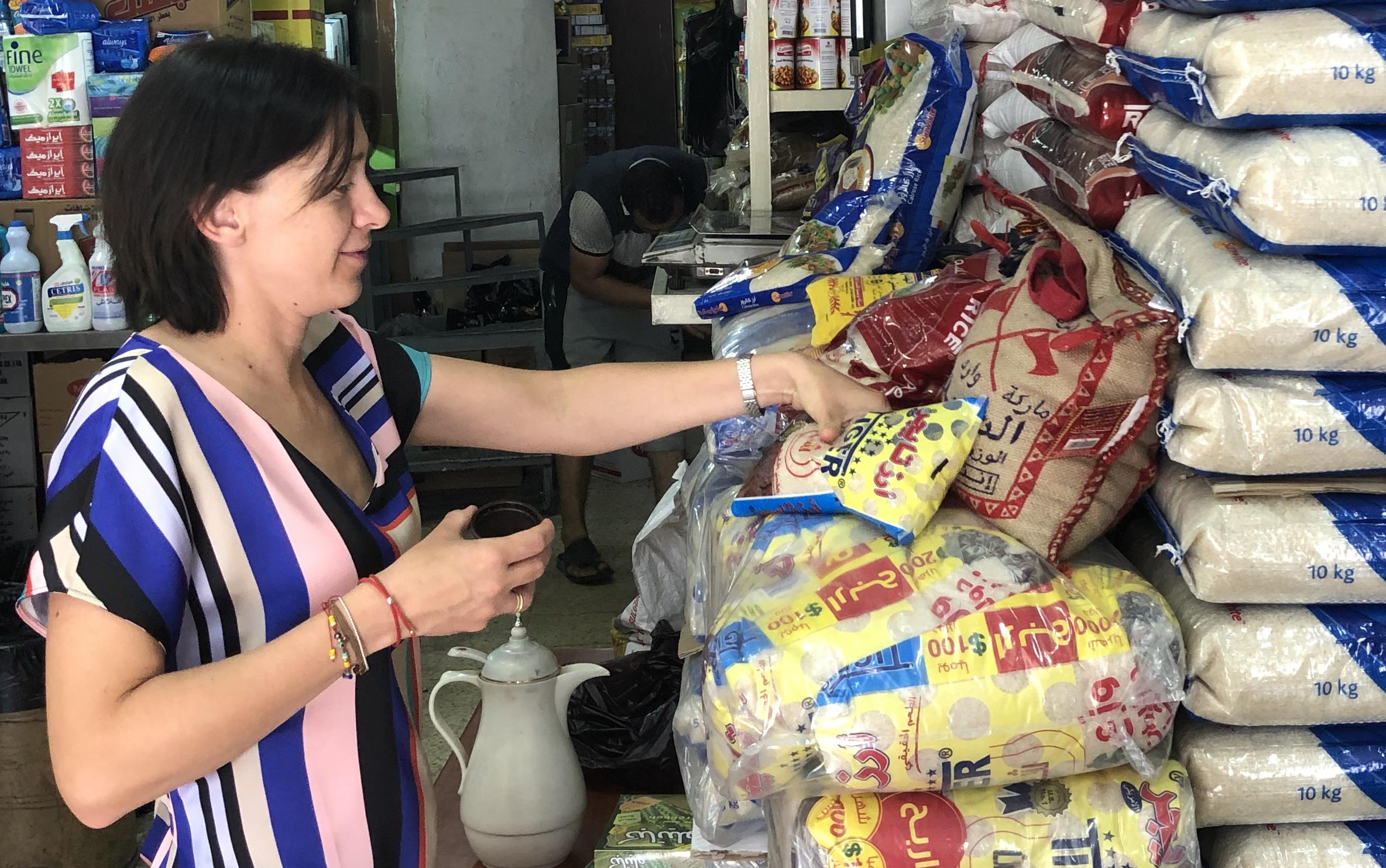 Woman wearing brightly striped shirt inspects rice brands in plastic bags, piled up to the ceiling