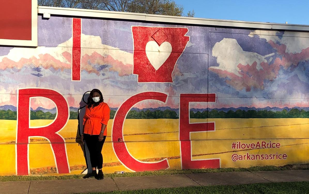 Black woman stands in front of I HEART Arkansas rice-mural