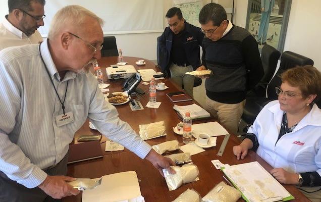 Rice samples in plastic bags inspected by group of people gathered around large wooden conference table