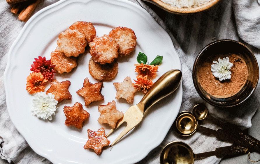 Pumpkin-Spice-Rice-Croutons on white plate surrounded by vessels filled with white rice, sugar, and spices