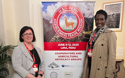 Vicki Manzoli & A. Grigsby stand in front of poster for USDA Peru Trade Mission