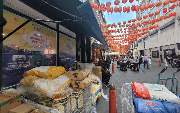 Orange lanterns strung above outdoor display with Mooncake Festival poster and bags of rice