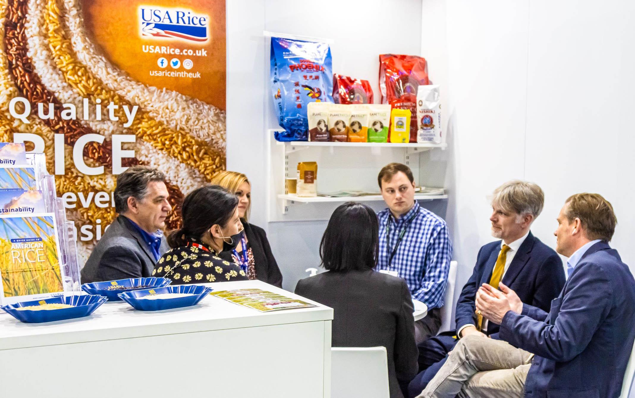 Group of people seated in trade show booth in front of rice poster, samples, and pamphlets