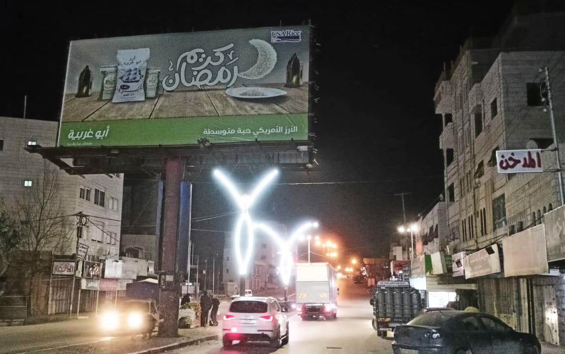 USAR billboard-in-the-West-Bank, nighttime urban scene with traffic and neon signs