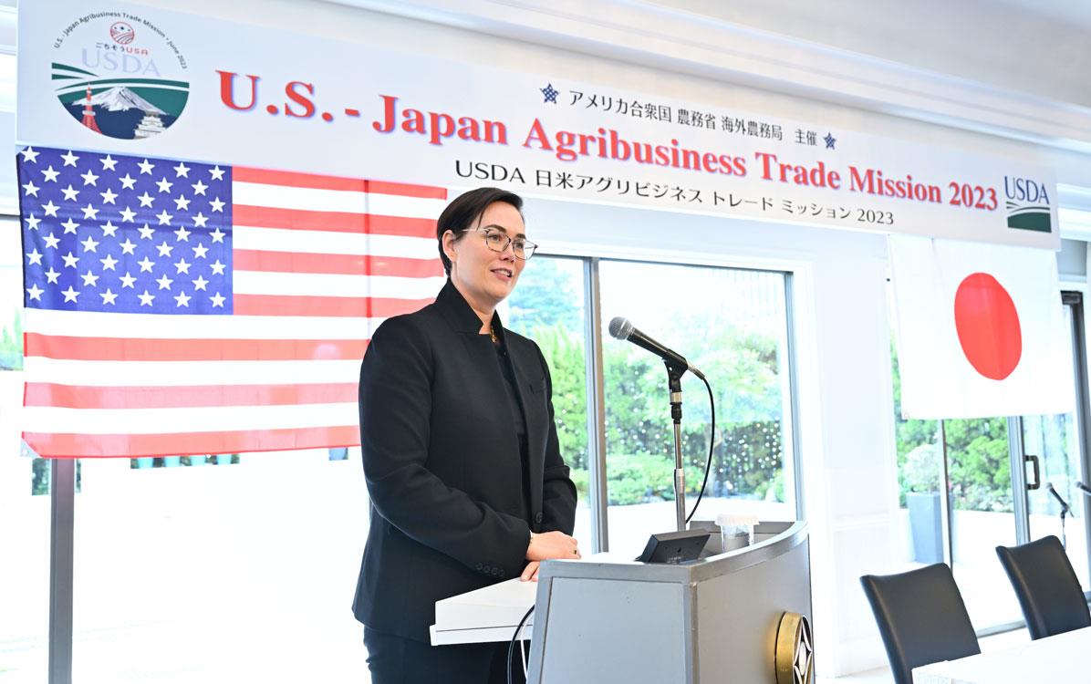 USDA-Under-Secy-Alexis-Taylor-at-podium in front of American & Japanese flags and welcome sign