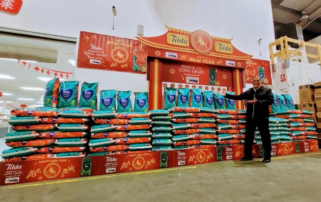 Man stands in front of colorful 2022 Year of the Tiger Tilda booth stacked with bags of US rice