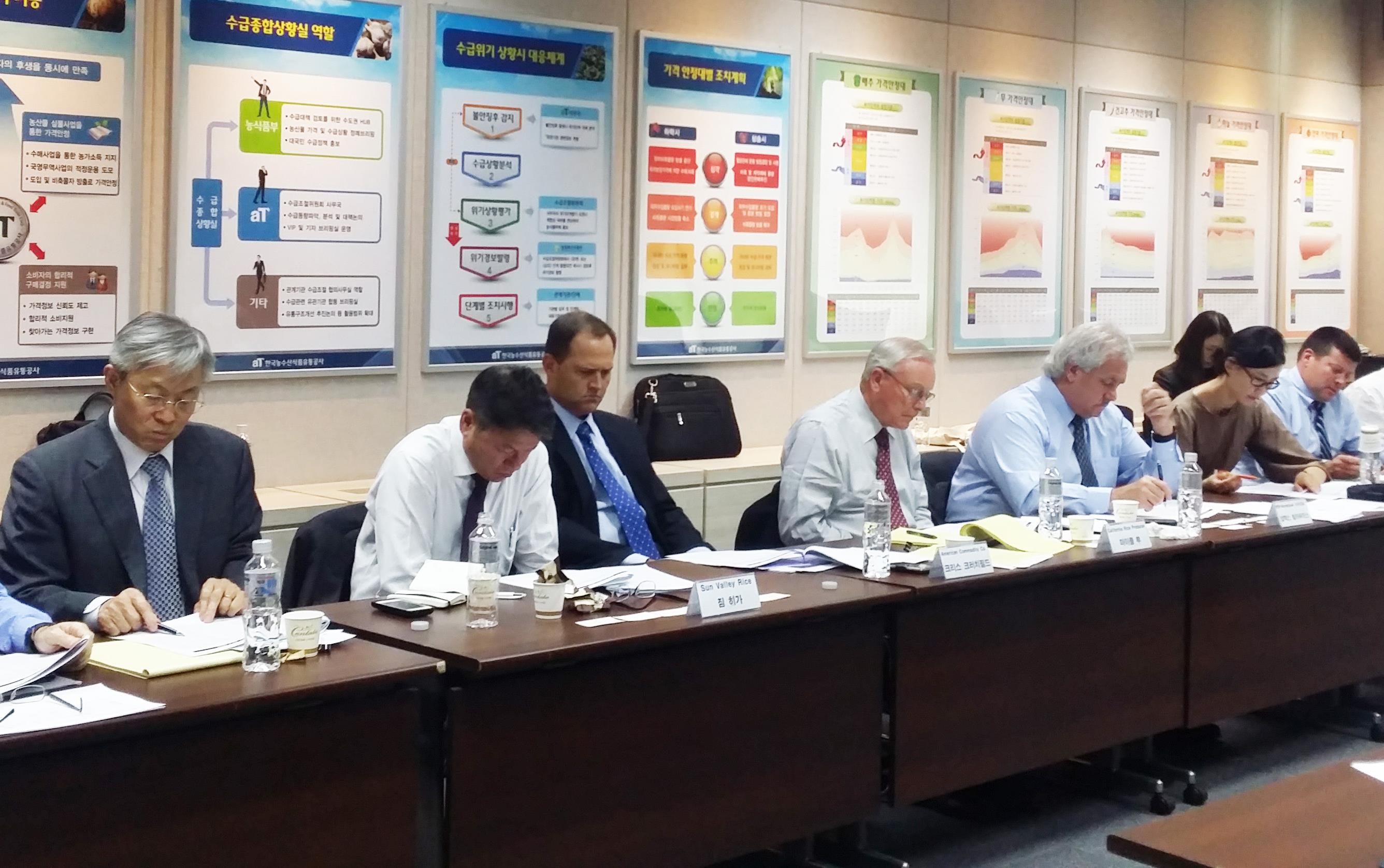 Men wearing business attire sit at a long table in front of wall of posters