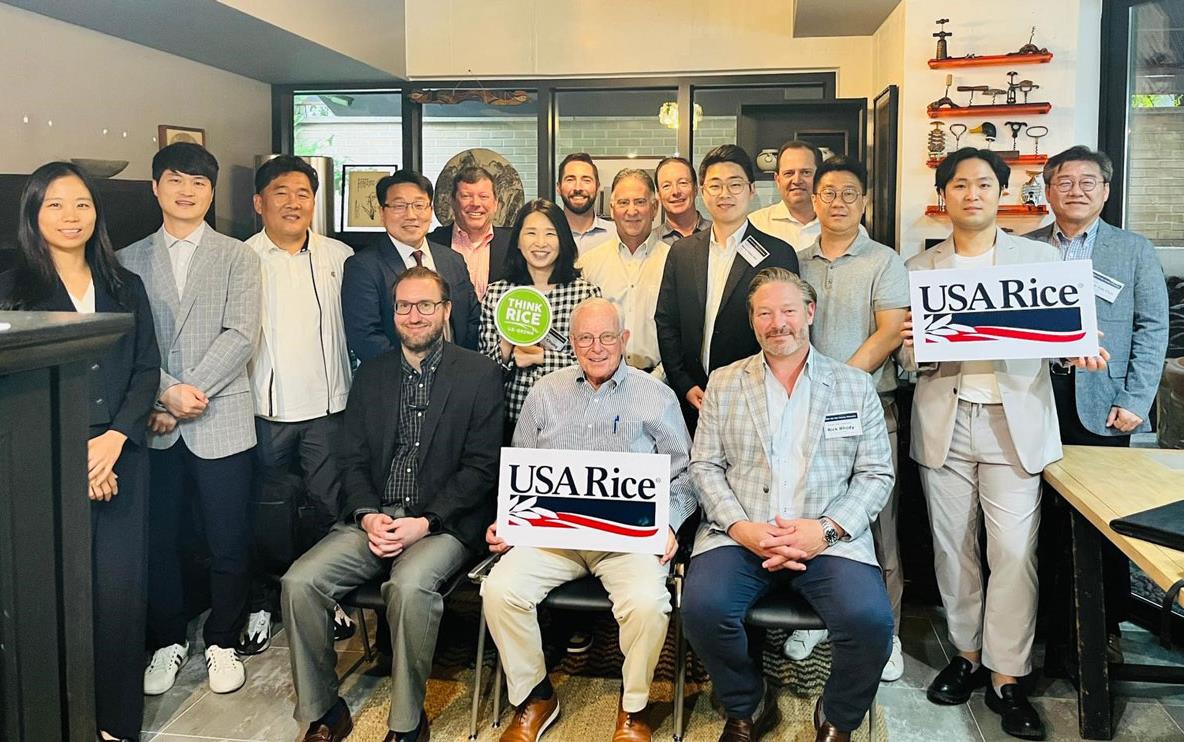 2023-Korea-Tech-Mtg,-group-shot of people seated and standing, some holding USA Rice signs