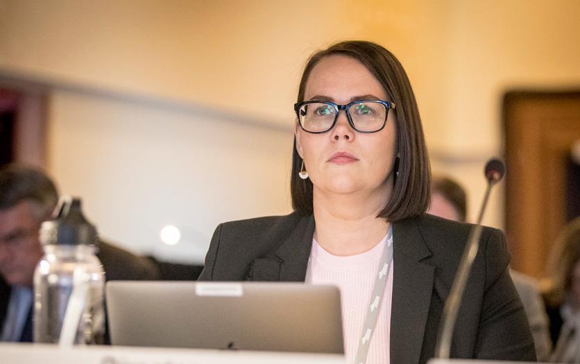 Alexis Taylor, Philip Gerlach photo, white woman w/dark hair and dark-rimmed glasses sits in front of computer & microphone