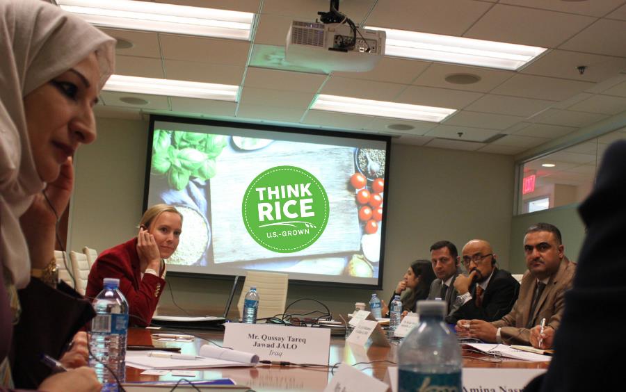 People wearing headphones sit around conference table, green Think Rice logo prominent on video screen in room