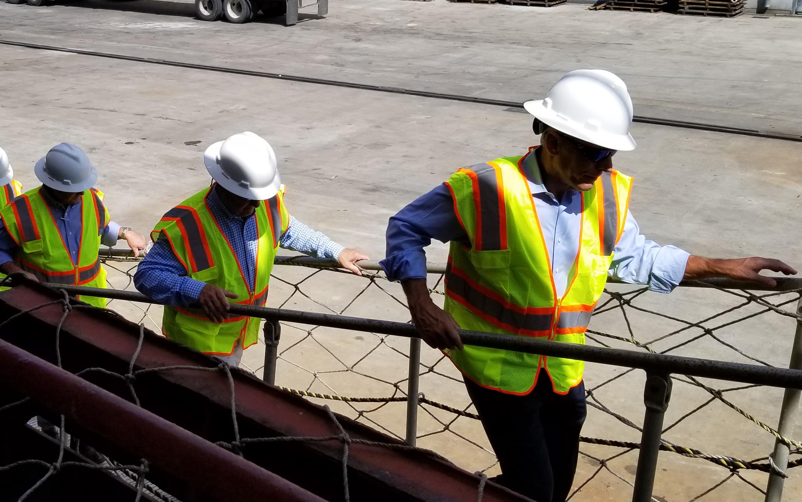 Line of people wearing fluorescent jackets and hardhats climbs the gangplank of a ship