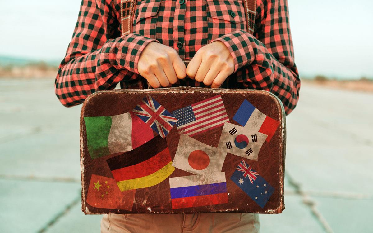 Person-holding-vintage-suitcase-with-international-flag-stickers