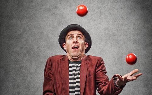 Man wearing burgundy suit and bowler hat juggles three red balls