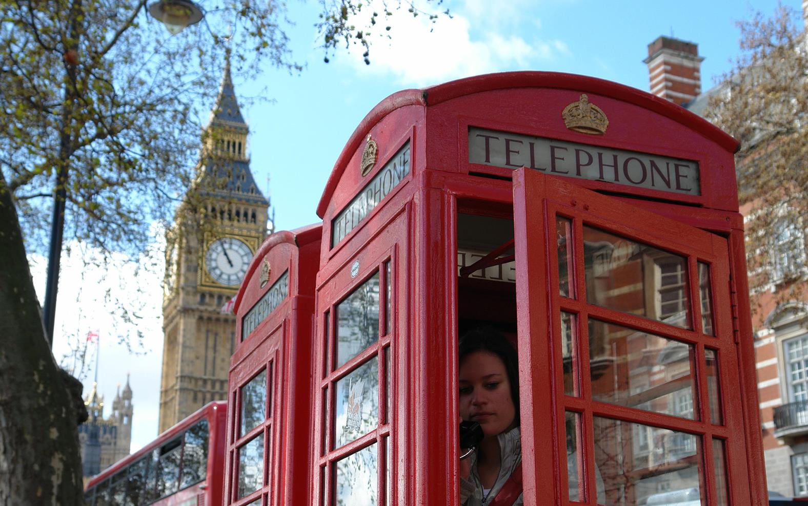 Woman on the phone inside a red UK telephone box, Big Ben in background