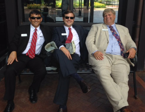 Three men wearing sunglasses and suits sitting on a bench