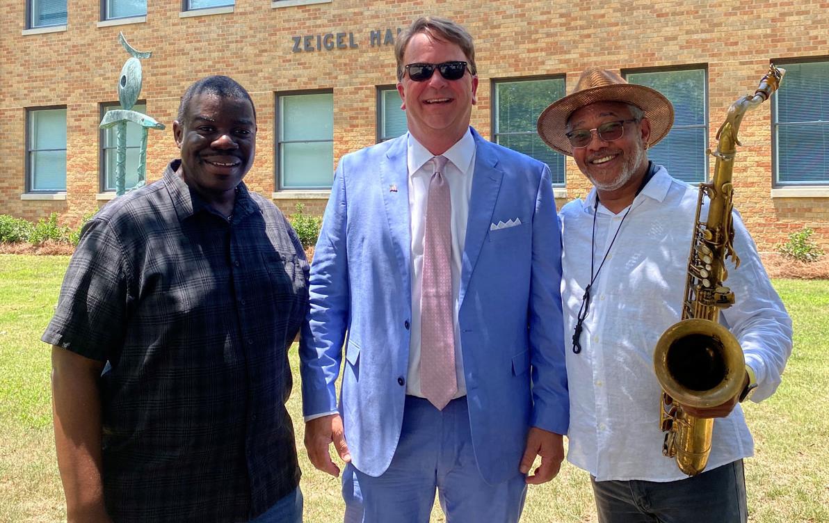 Two Black men flank a white man wearing a business suit, man on right is holding a saxophone