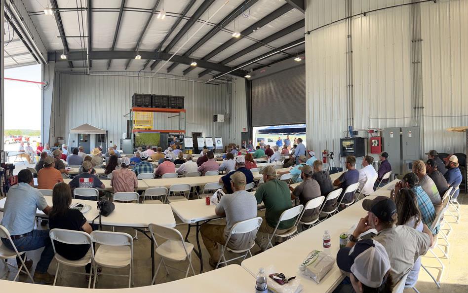 Panorama view of people sitting at tables listening to presentation inside large metal building