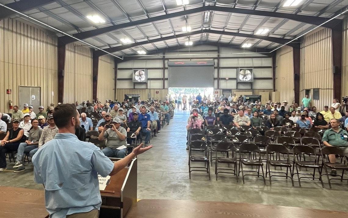 2024 LSU Field Day, Peter Bachmann stands at podium addressing crowd in farm bldg