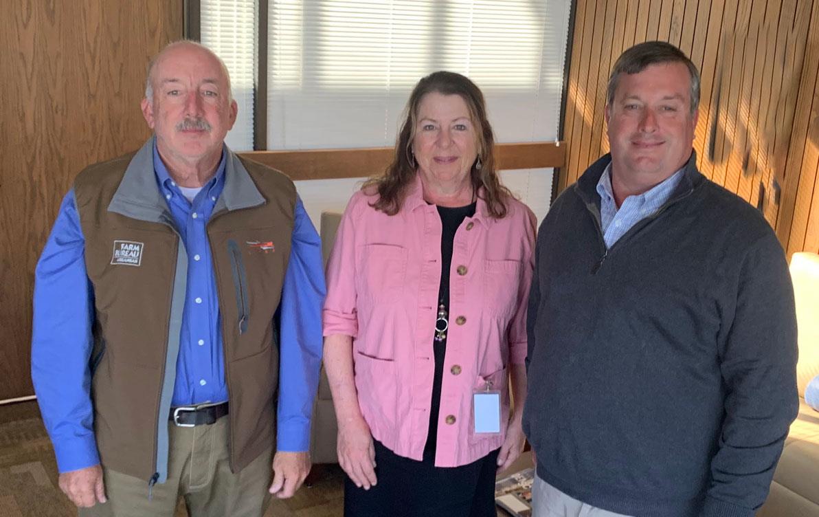 Three white people, two men flanking a woman wearing a pink jacket