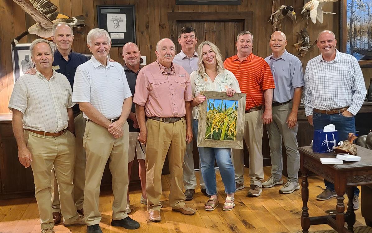 Brandy Carroll holds painting given to her by Arkansas rice leadership who are gathered around her