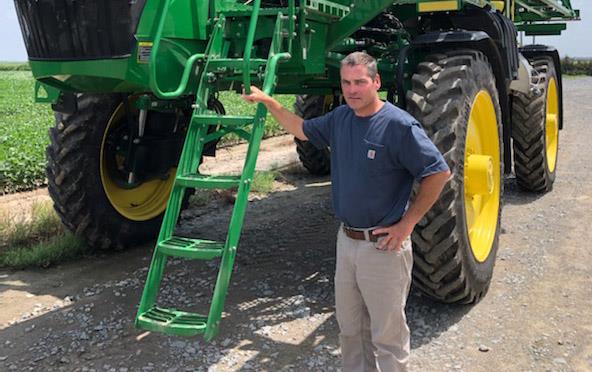 Man holds onto ladder of green pesticide sprayer