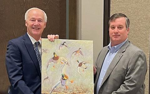 Two white men wearing business suits hold painting of ducks in a rice field