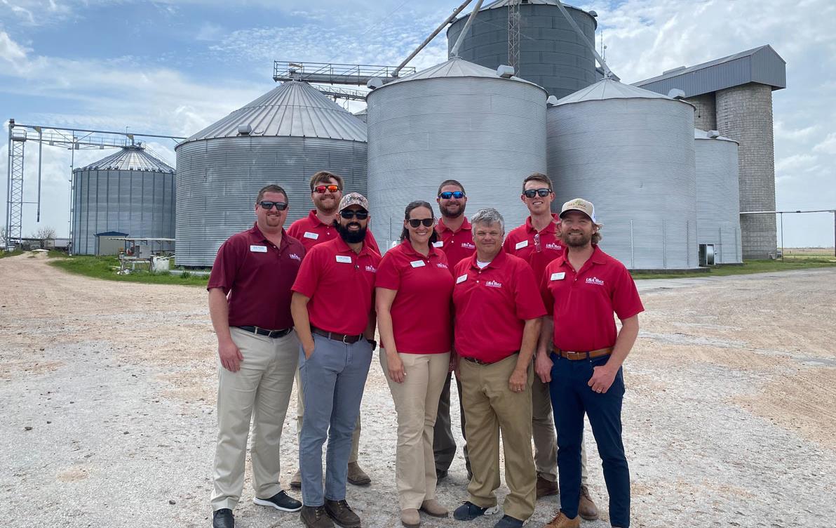 Group of people wearing red shirts stand in front of grain bins