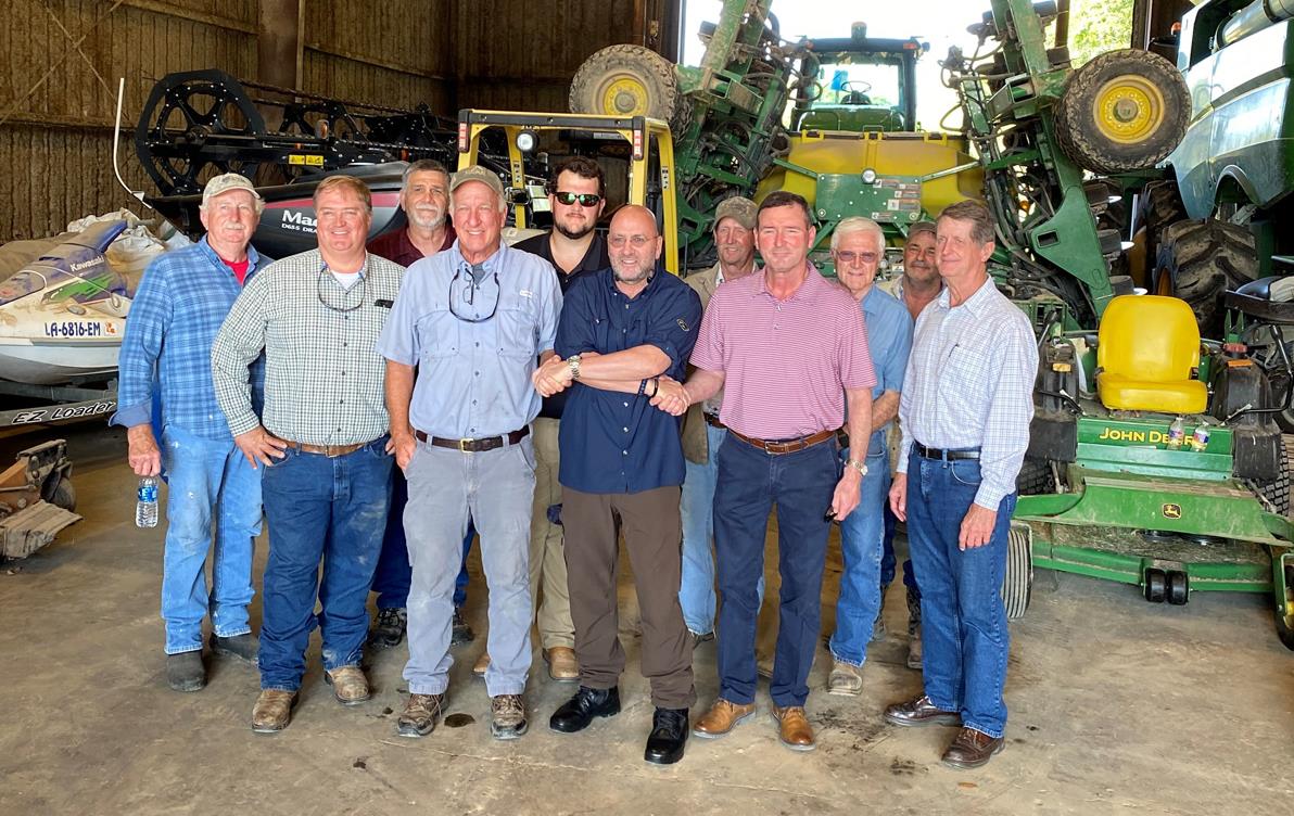 Group of men stand in farm shop in front of farming equipment