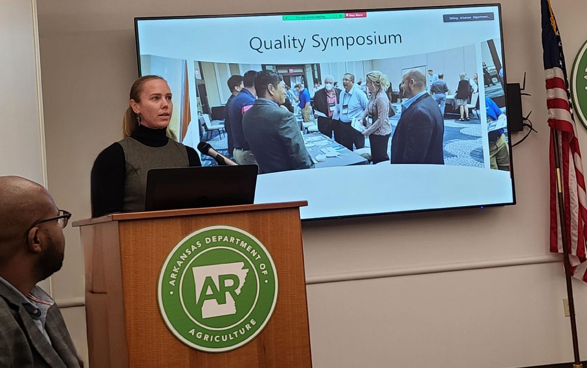 Sarah-Moran-at-podium-at-ARR&P-Bd-mtg with slide presentation on screen in background