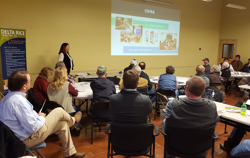 Woman gives slide presentation to crowd of people seated around tables