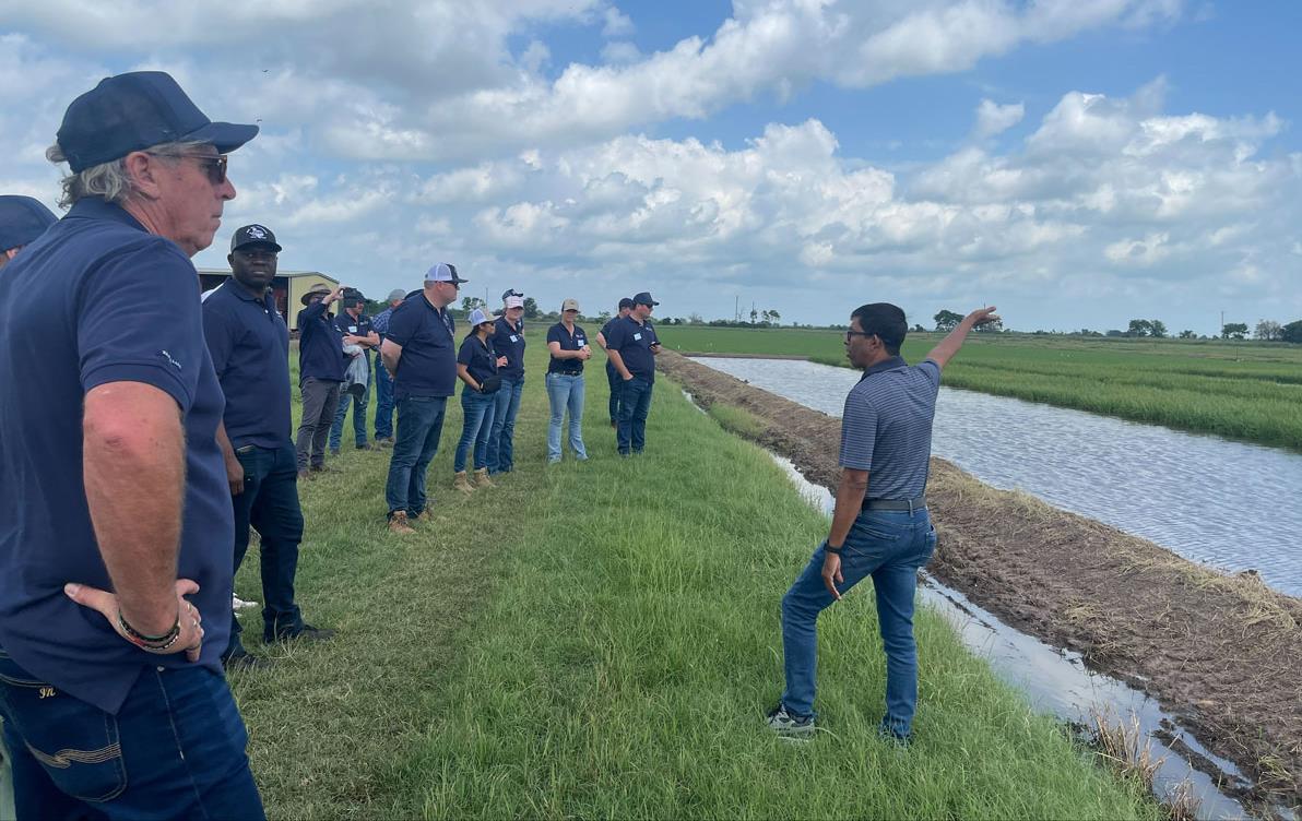 Australians-at-Eagle-Lake,-TX, standing near flooded rice fields with one person in front pointing to sky
