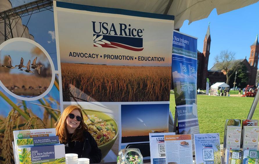 #AgDay22 on the National Mall, USA Rice booth with smiling woman seated behind table