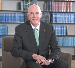 USDA FAS Admin Ken Isley, middle-aged, bald, white man wearing suit, sitting in chair in front of bookcase