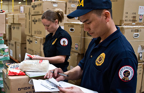 FDA inspectors holding clipboards in warehouse filled with boxes of food products