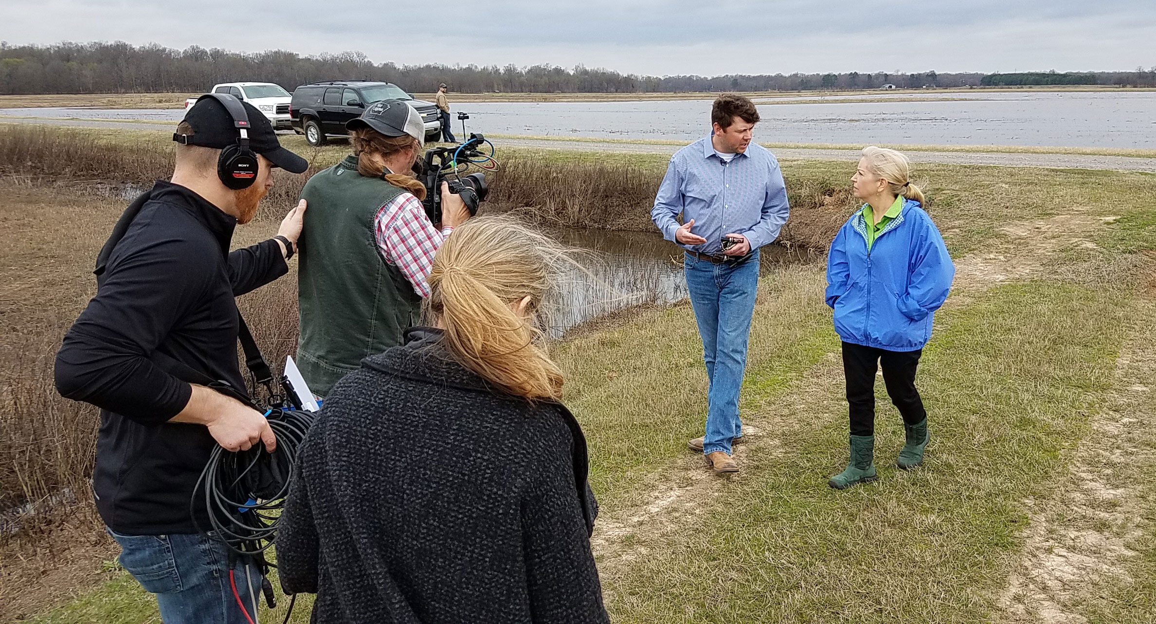 AR Sara-Moulton-Shoot-Sara-&-Eric-Vaught-being filmed by camera crew while walking outside near flooded rice field