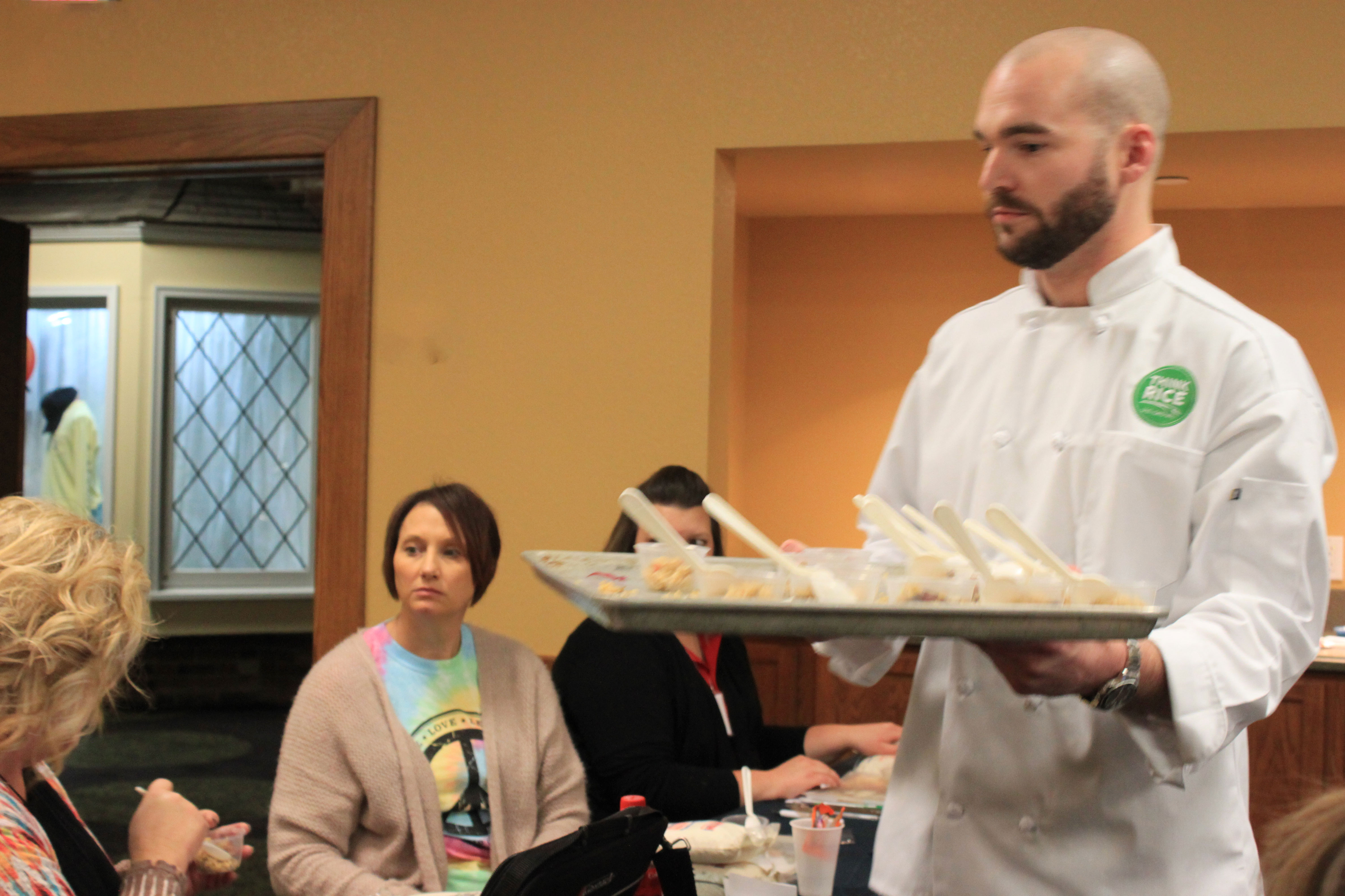 Chef-Charles-Dottore-distributes rice dish samples on a tray to teachers seated at tables