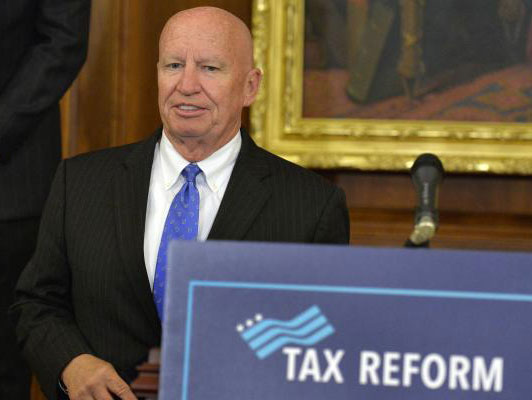 Rep-Kevin Brady-standing next to podium with "Tax Reform" sign