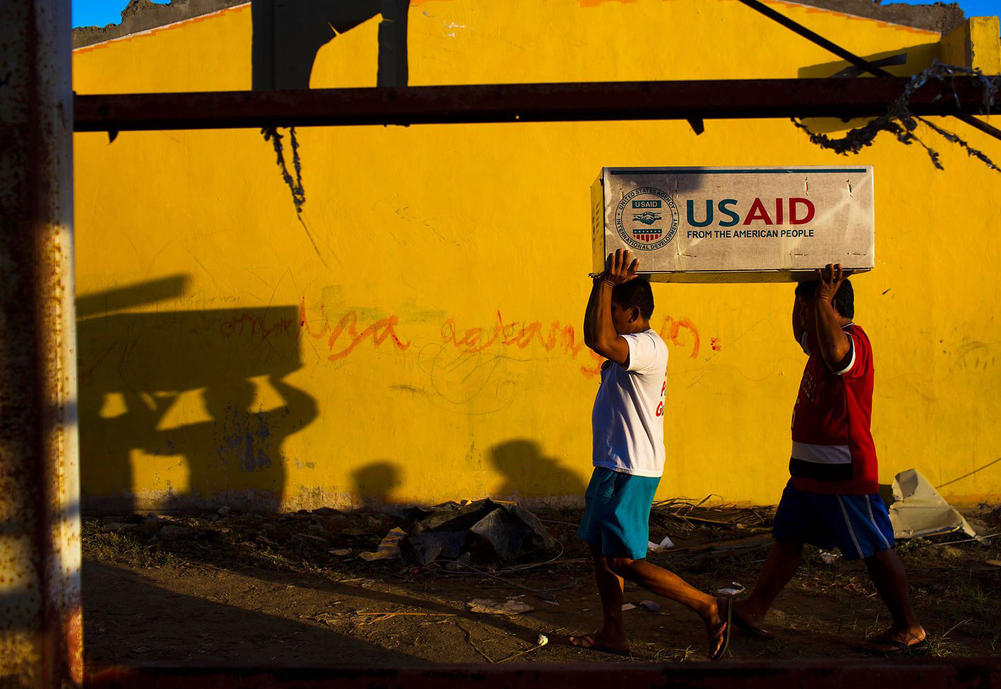 Two men balance a box of USAID food aid on top of their heads