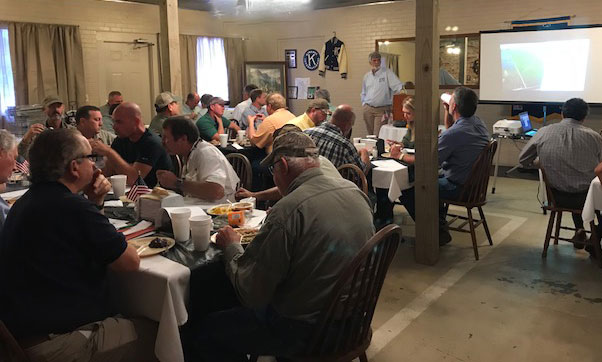 Meeting with farmers sitting around tables, listening to presenter, eating dinner