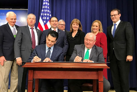 USDA & FDA sign agreement to bolster coordination, two men seated at table signing document with others standing behind them