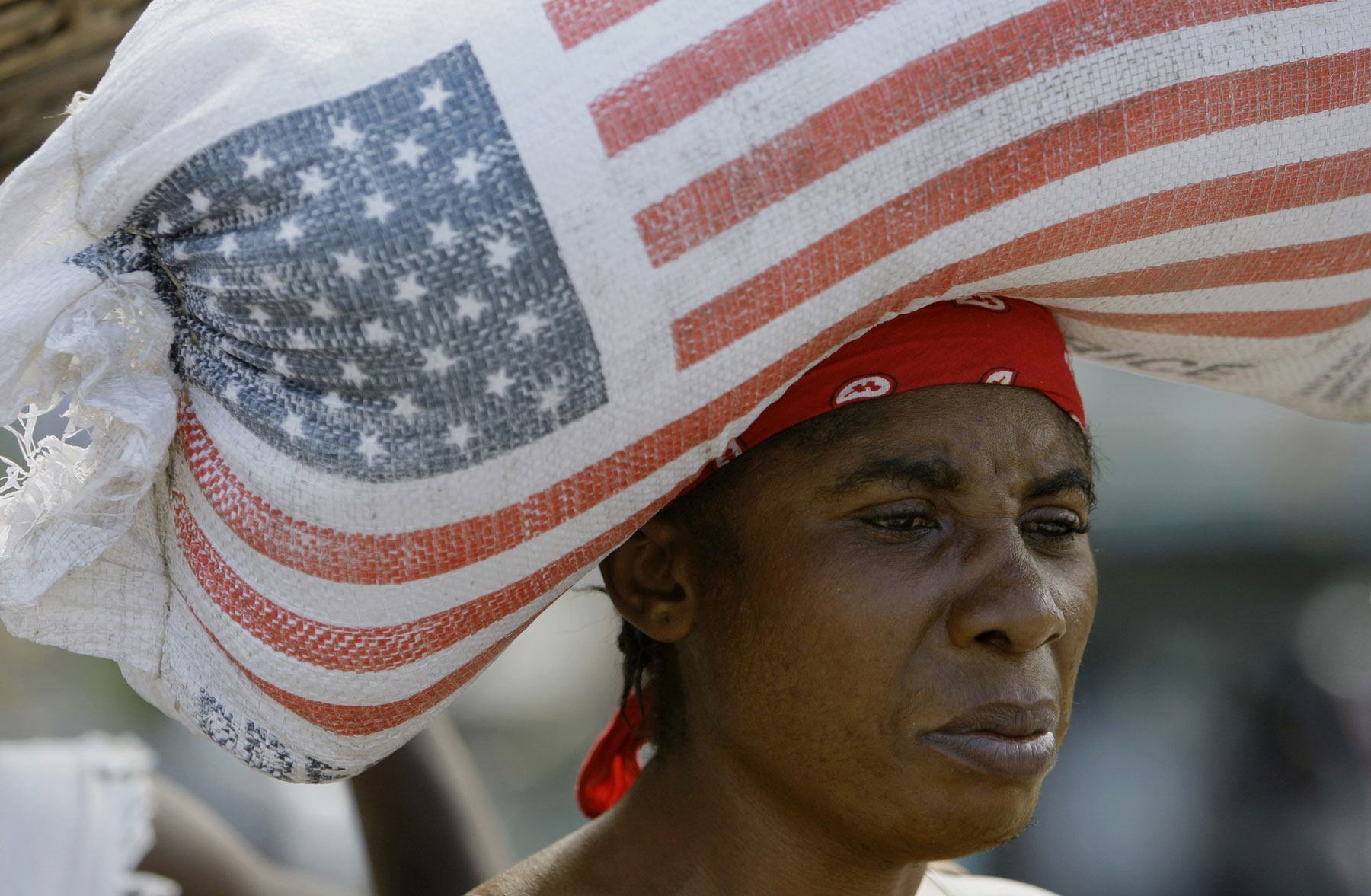 Dark-skinned woman carries bag of US rice on her head