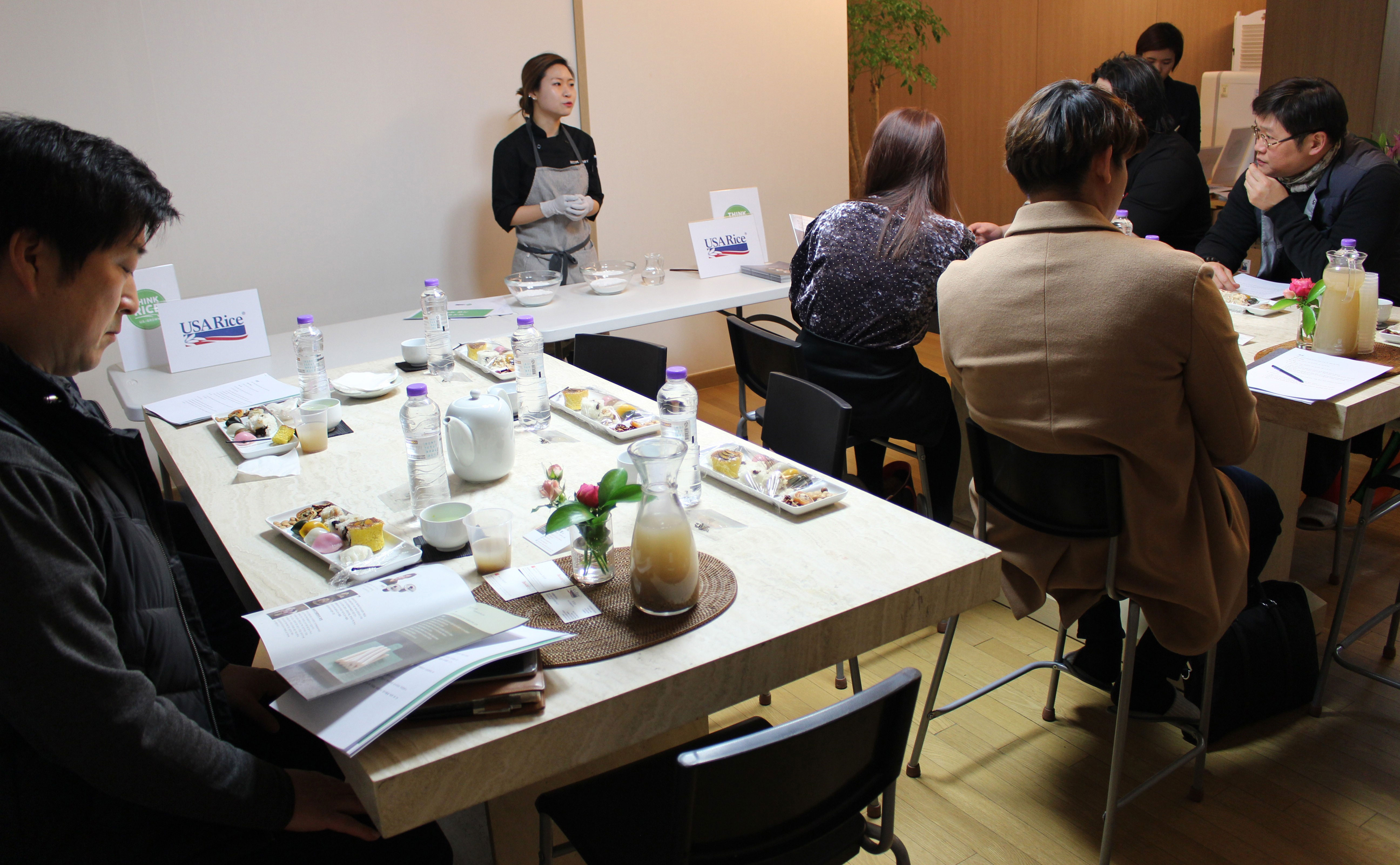 Female chef gives cooking seminar for participants at tables filled with ingredients