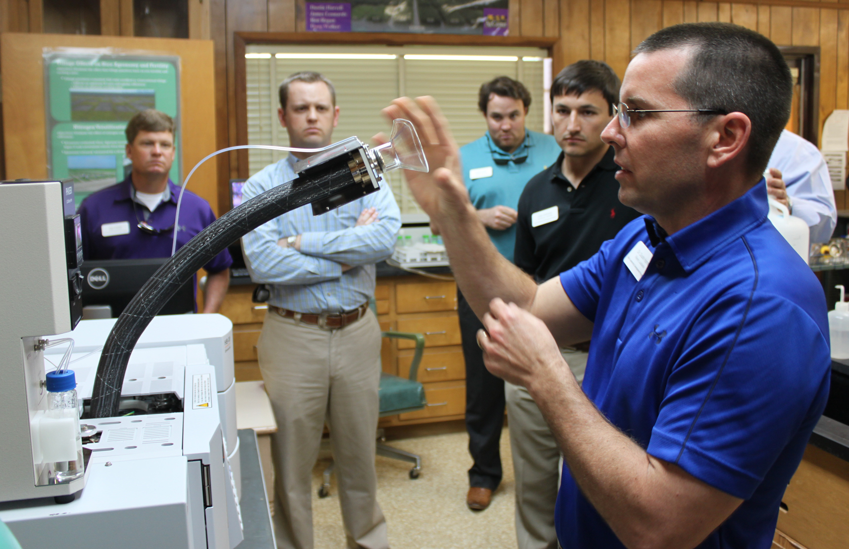 Man demonstrates lab equipment to group of men watching