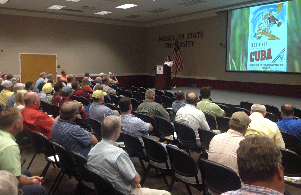 Large group seated in chairs listens to CEO Betsy Ward give a presentation from a podium on trade with Cuba